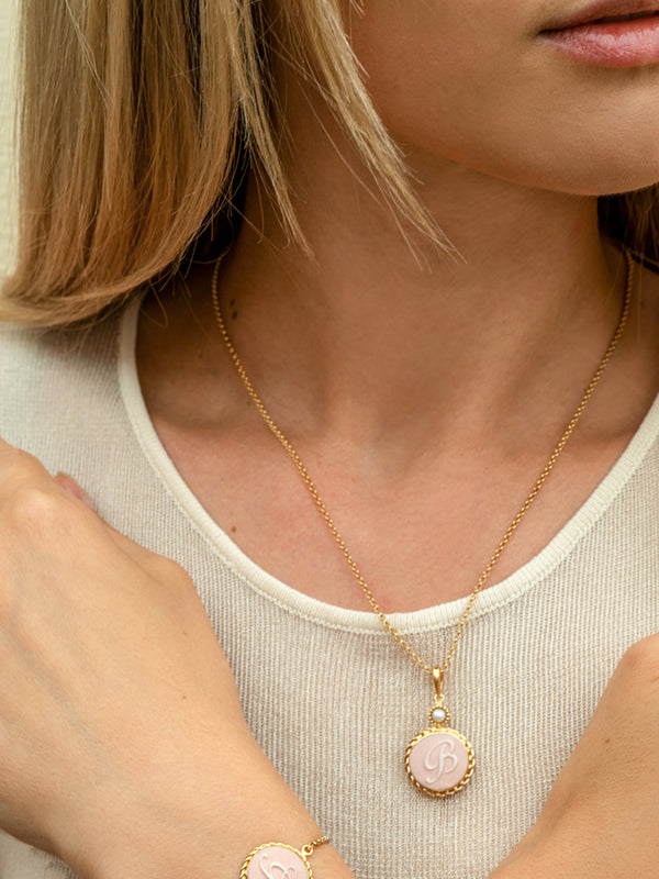 A close-up shot of a young lady wearing a pink cameo necklace styling an engraved B letter