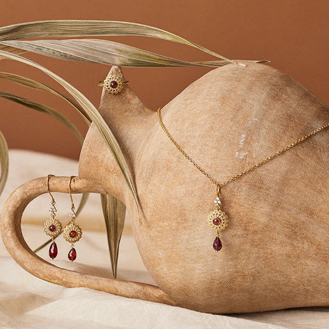 Gold-plated jewelry set with garnet — ring, earrings and necklace — styled on a ceramic vase with dried palm leaves, part of Vintouch Gifts Under €150 collection.