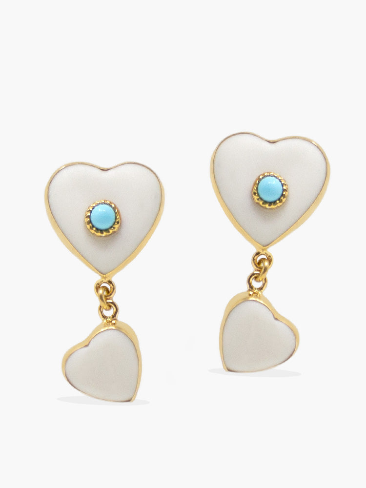 Heart-shaped earrings in white porcelain set in gold vermeil, featuring a turquoise cabochon in the middle. A smaller heart pendant dangles below. 